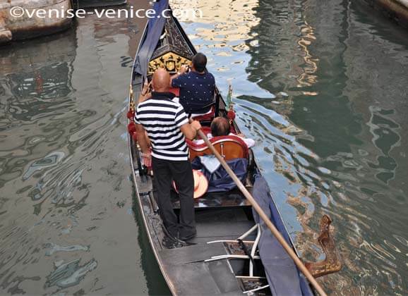 Une gondole sur un rio,le gondolier emmene 2 touristes qui prennent des photos de venise