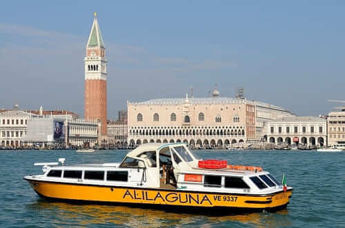A venise, un vaporetto Jaune alilaguna dans le canal de la Giudecca avec le palais des doges et le campanile saint-marc en arrière-plan.